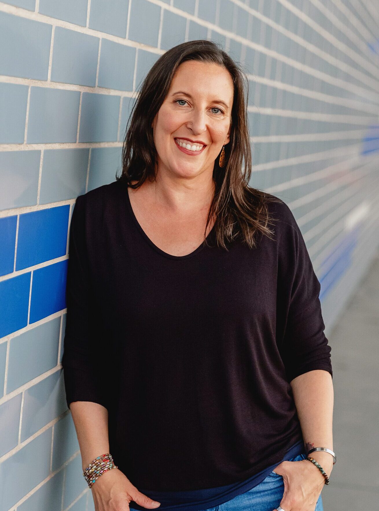 Kristeen leans against a blue wall, smiling